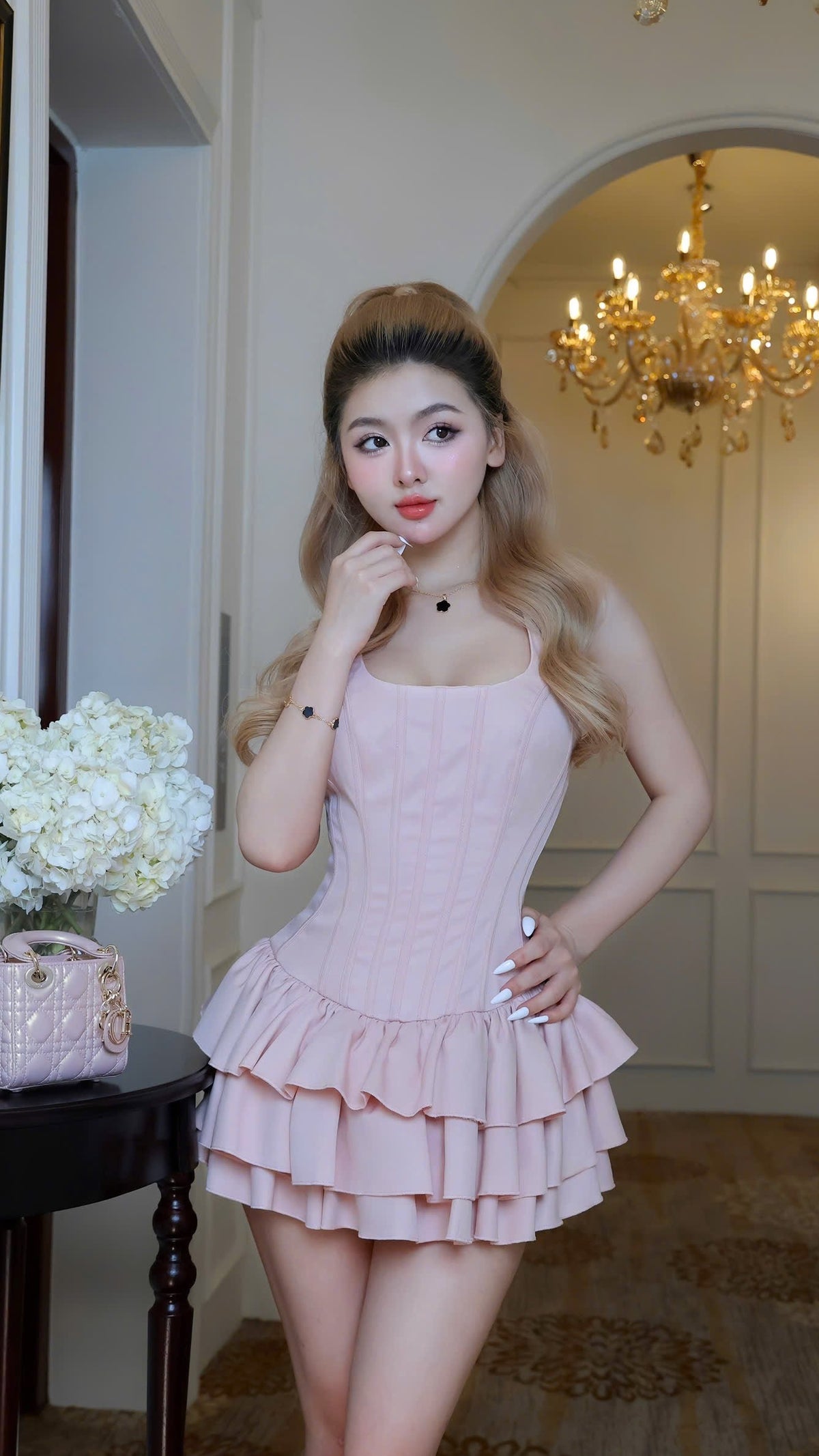 Woman in a pink dress standing in an elegant room with a chandelier.